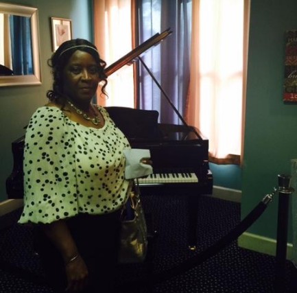 Mrs. Edna Youmans standing next to a piano